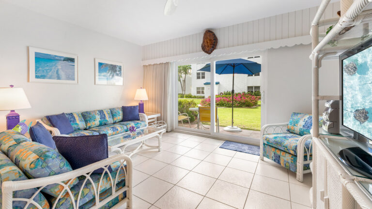 The living room of first floor Villa 3, Grand Cayman Vacation Rental with a view of the gardens and patio and umbrella.